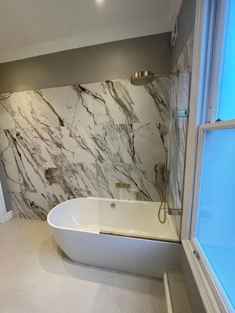 Freestanding bath beneath a marble feature wall with brushed brass rainfall shower