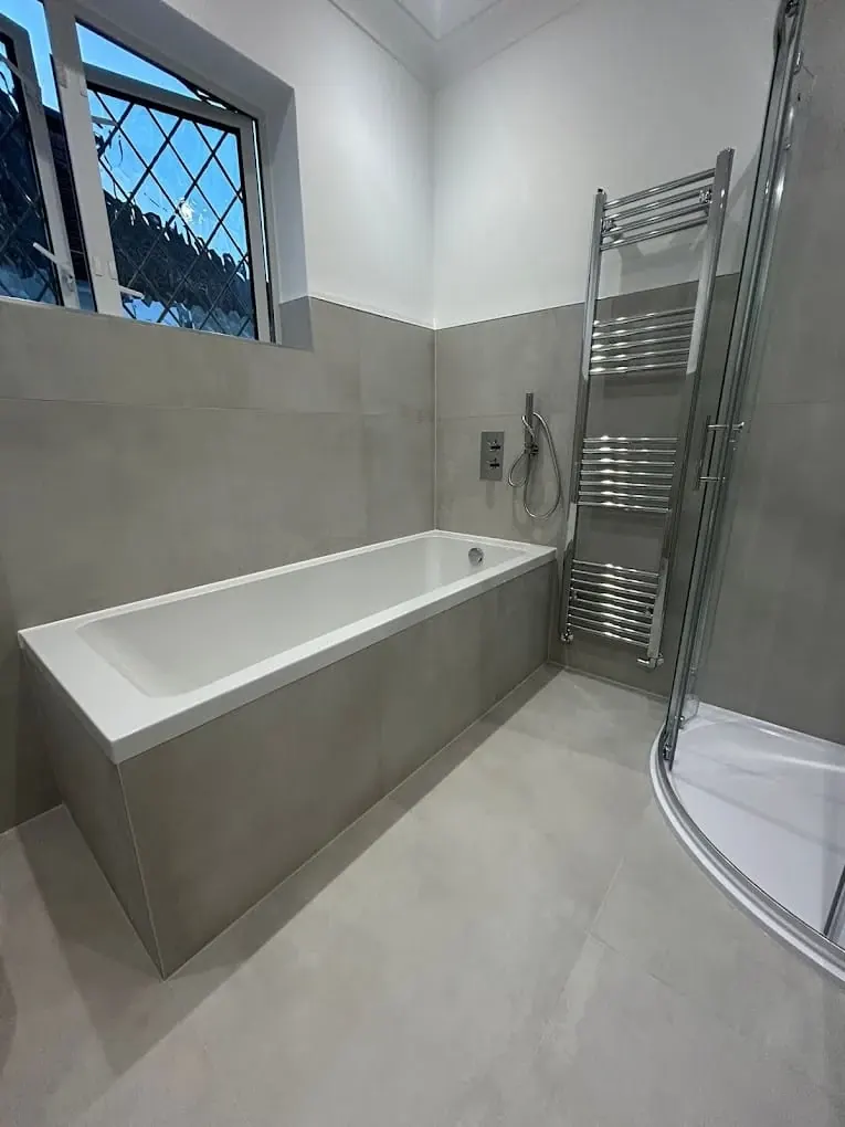 Grey-tiled family bathroom with straight bath, chrome towel radiator and corner shower